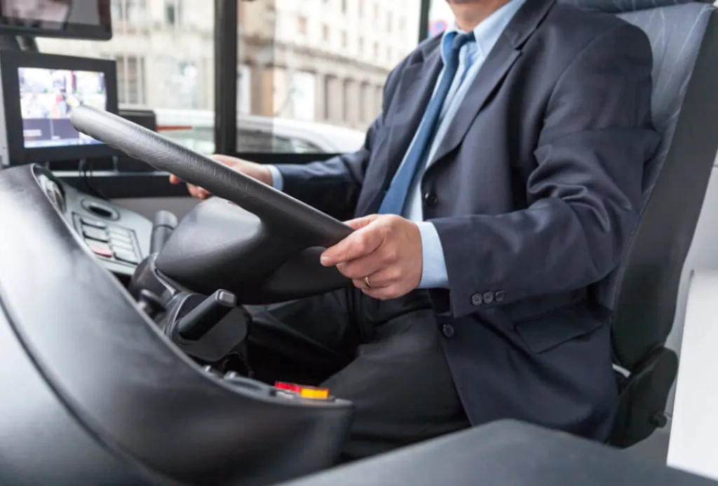 Bus driver in a suit holding the steering wheel inside a modern coach bus.