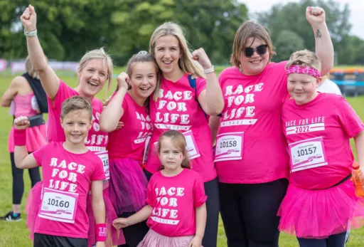 Group in pink 'Race for Life' shirts posing and cheering at an outdoor charity event.