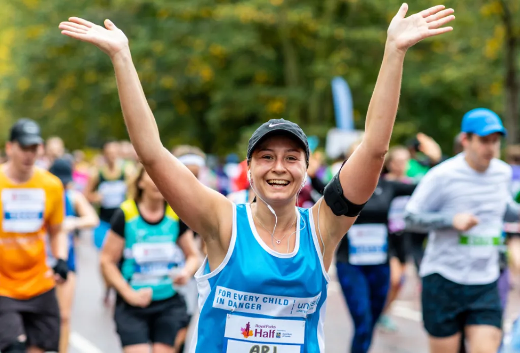 Smiling woman raises arms while running a charity race in a crowd of participants.