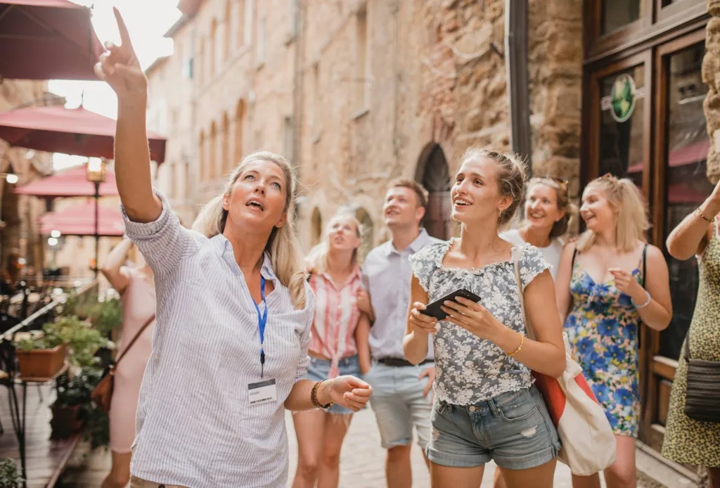 Tour guide pointing out sights to a smiling group in a historic European street.