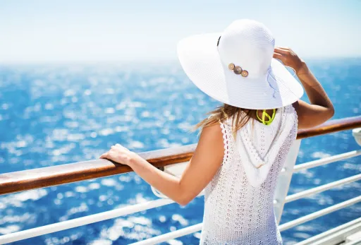 Woman in sunhat enjoying ocean view from cruise ship deck on a bright, sunny day.