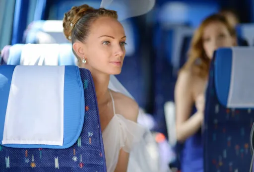Bride in a white dress sitting on a coach bus, looking ahead with a calm, focused expression.