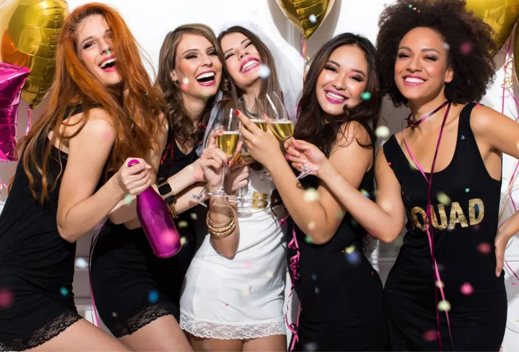 Bride-to-be celebrating with friends at a hen party, holding champagne and smiling.