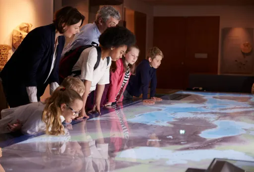 Group of children and adults studying an interactive map display in a museum exhibit.