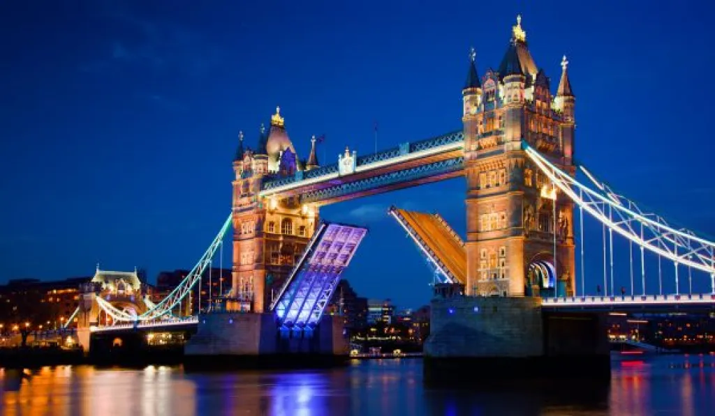 Tower Bridge in London lit up at night with its bascules raised over the River Thames.