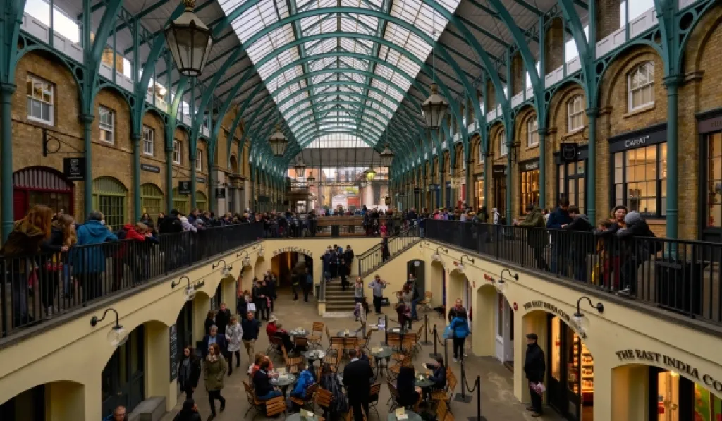 Busy Covent Garden Market in London with shops, cafes, and people on both levels.
