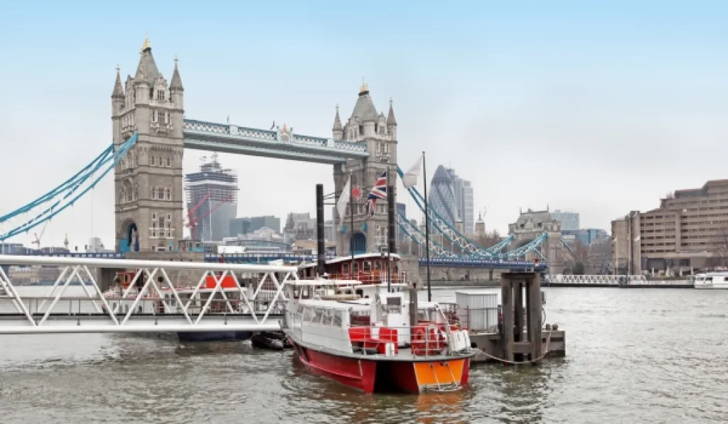 Tower Bridge in London with a red and white tour boat docked on the River Thames.
