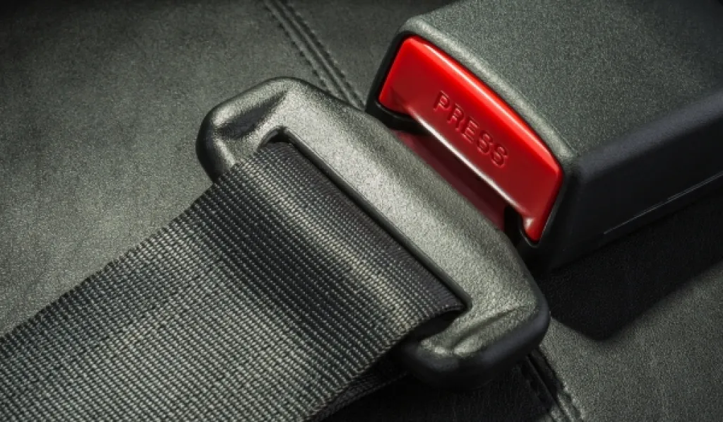 Close-up of a black seatbelt fastened into a red buckle on a leather seat.