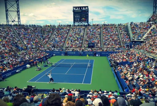 Packed tennis stadium during an Open match with player serving on blue hard court.