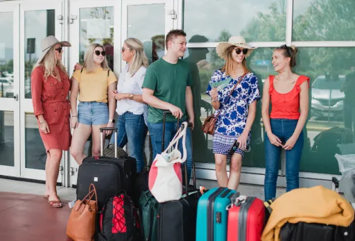 Group of travelers with luggage outside airport terminal, ready for holiday trip.