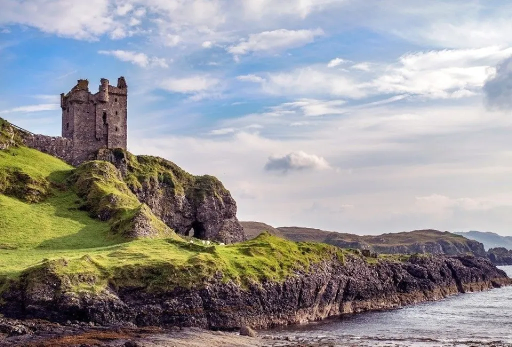 Scenic coastal castle ruins in Scotland on rocky cliffs with ocean view and green hills.