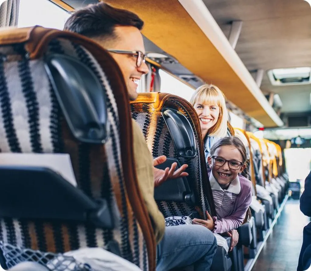 Smiling family enjoying a coach journey with child leaning forward in patterned seats.
