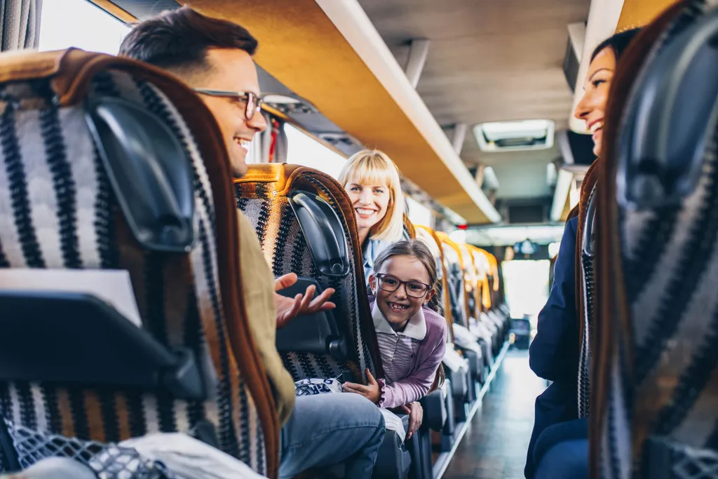 Smiling family enjoying a coach journey with child leaning forward in patterned seats.